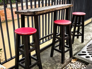 Outdoor bar stools with a red seat and a wooden table near a fence