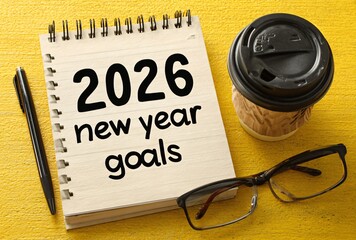 Setting 2026 new year goals on a notebook with pen, coffee, and glasses.