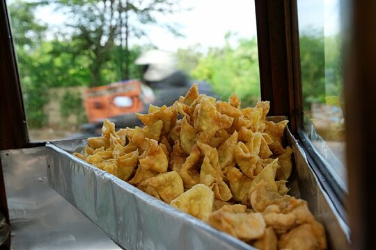 A tray of golden crispy Indonesian fried dumplings or pangsit goreng displayed at a food stall near a window