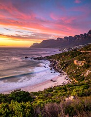Coastal vista captured at dusk, revealing a long beach nestled between a rugged coastline and mountains under a vibrant, painted sky