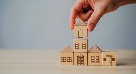 Hand stacking wooden blocks to build a house model on a table.