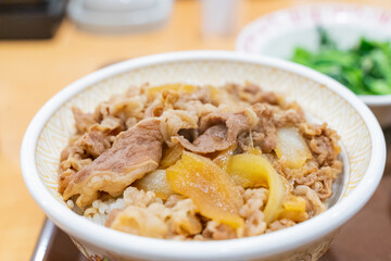 A Japanese beef bowl set meal from Sukiya, featuring simmered sliced beef over steamed rice, served with fresh vegetables and side dishes. The presentation highlights traditional Japanese fast food wi