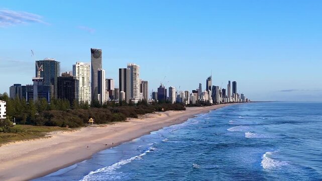 Drone glides north along the coast toward Broadbeach, passing over rolling waves, golden sand, and sleek beachfront high-rise apartments.