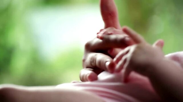 mother holding her baby's hand outdoor in the garden. trust, care or bonding concept. woman and her infant child in a backyard together in summer day.