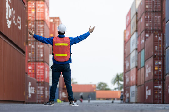 Back view of logistics worker in safety gear raising arms at container yard, symbolizing success, achievement, teamwork, cargo coordination in the global shipping industry. - Powered by Adobe