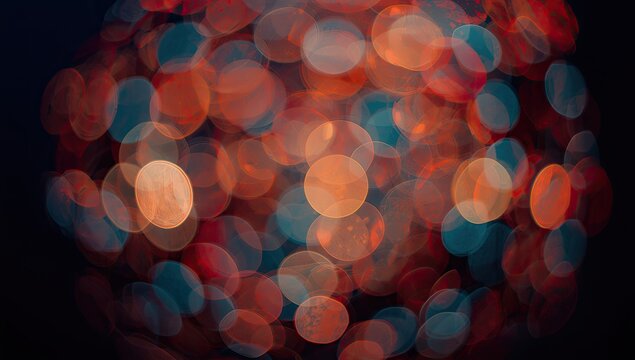 Abstract bokeh photograph features a cluster of luminous, circular shapes in warm orange, red, and cool teal hues against a dark, blurred background, creating a soft and dreamy effect that is...