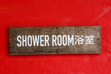 Obraz premium Rustic wood sign with white text for shower room in english and chinese hangs on bold red wall background. simple, clear direction has vintage feel