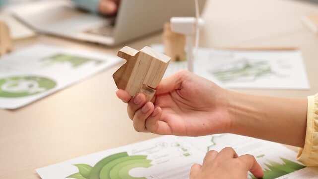 Excellent business people analyzing on eco house project at messy table with green energy using graph with windmill, home, tree model to decrease carbon usage, save earth. Focus on hand. Delineation.