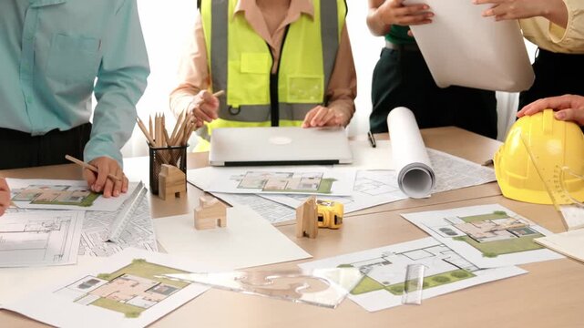 Smart architect and safety engineer discussion about building blueprint on table with architectural document, measurement tools and wooden block scatter around at modern office. Closeup. Delineation.