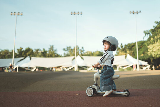 Cute little child wearing helmet riding small tricycle scooter in outdoor park, toddler playing and learning balance in natural, family lifestyle childhood development concept with safety awareness - Powered by Adobe