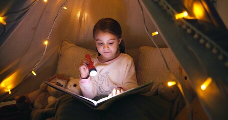 Child, torch and reading book in tent at night for fairytale, bedtime storytelling and literature. Kid, flashlight and fantasy novel with folklore story, imagination and language development at house