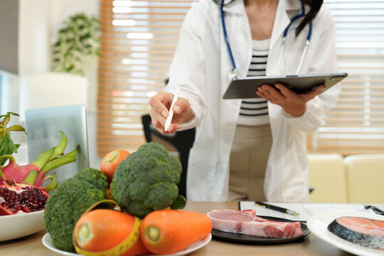 Professional nutritionist plans healthy diet with fresh vegetables and fruits while writing notes in a bright modern office setting. - Powered by Adobe