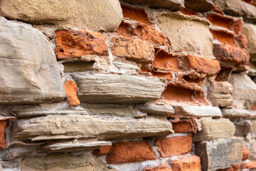 Old brick and stone wall texture with irregular pattern. Weathered masonry surface showing red bricks and natural sandstone blocks in rustic construction style.