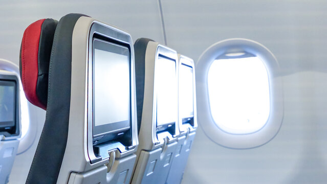 Airplane interior featuring empty passenger seats with personal screens and a bright window, creating a serene travel atmosphere with copy space