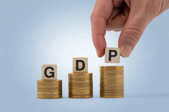 Hand placing the letter p onto a coin stack next to g and d, completing the gross domestic product gdp acronym