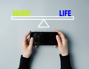 Hands holding smartphone on scale balancing work and life text on gray background balance High Quality Image