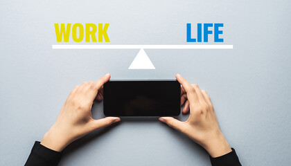 Hands holding smartphone on scale balancing work and life text on gray background balance High Quality Image