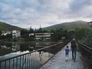 Fototapeta premium Father and son walking on a bridge in a mountain park with a small lake