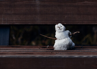 A small snowman stands on a bench.