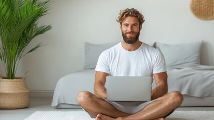 Man with laptop sitting cross legged on floor smiling at home