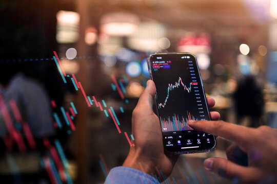 A person is holding a cell phone and pointing at a graph on the screen