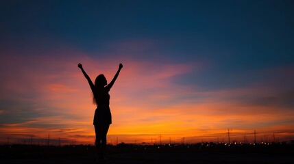 Fototapeta premium A silhouetted figure celebrates against a vibrant sunset, embodying joy and freedom in a serene outdoor setting.