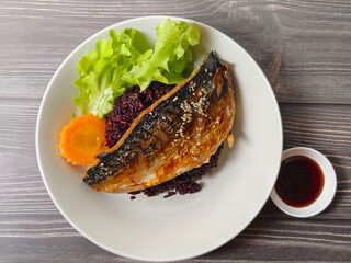 Delicious steamed mackerel with soy sauce on black rice, topped with sesame and served with lettuce and carrot. Healthy homemade Asian food concept.