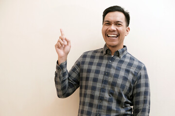 Fototapeta premium Southeast Asian man wearing flannel shirt cheerful expression pointing to the right side with excited expression, on white isolated background