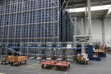 Modern automated warehouse with high-rise racks filled with blue containers. Logistic center with metal shelves, conveyor systems, and packing stations.