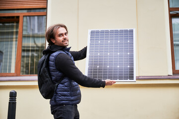 Man holding photovoltaic solar panel in front of historical building. Concept of integration of sustainable renewable energy sources into architecture.