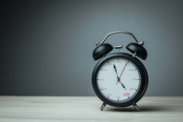 The hands of clock point to June on dial black alarm clock with copy space. Concept of monthly goal planning, important appointments and effective time management.