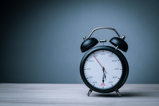 The hands of clock point to July on dial black alarm clock with copy space. Concept of monthly goal planning, important appointments and effective time management.