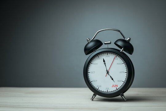 The hands of clock point to June on dial black alarm clock with copy space. Concept of monthly goal planning, important appointments and effective time management.