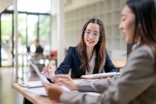 Businesswomen working together on project in office meeting discussing documents smiling and analyzing charts