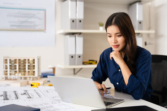 Young female engineer designer or contractor working on drawing plans analyzing structure on laptop computor at construction site office. copy space.