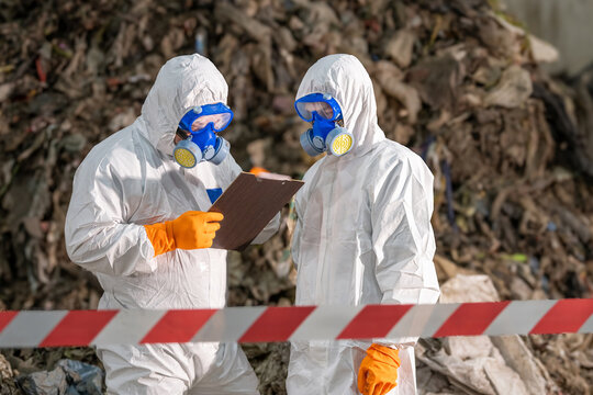 Two scientists in protective suits and masks analyzing documents outdoors in hazardous environment with warning tape and rocky background for safety research or environmental study