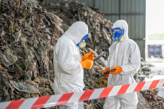 Two scientists in full protective gear conducting environmental sampling or research at a contaminated site with rocky terrain, safety equipment, and caution tape