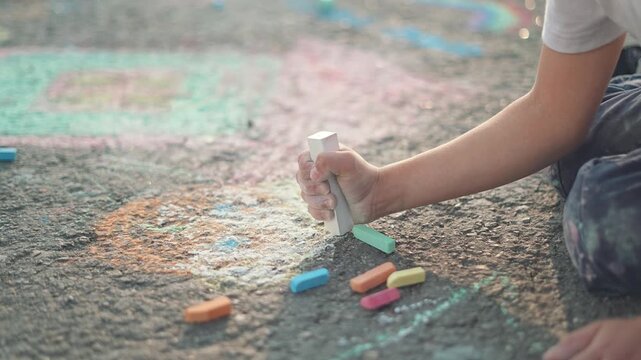 A child hand uses chalk to make colorful and detailed drawing on the street. Outdoor play turns the kid bright ideas into art. Chalk spreads color, the street changes, and the child enjoys creating.