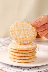 Hand Holding Crispy Japanese Senbei Rice Crackers Stack on White Plate - Traditional Asian Snack Food