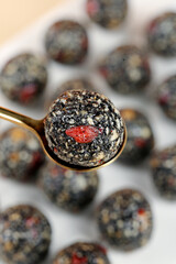 Handmade Black Sesame Seed Energy Balls with Dried Fruit on Golden Spoon - Healthy Nutritional Snack Closeup