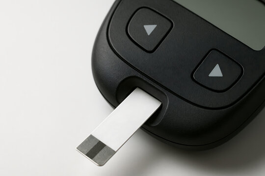 Macro view of a digital glucometer with a white test strip inserted, symbolizing blood sugar testing and precise medical monitoring for diabetes.