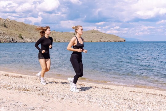 Two women jogging along a scenic beach on a sunny day near the water