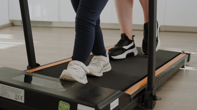 Mom and small girl walking side by side on treadmill at home. Family fitness, healthy lifestyle, and active parenting concept.