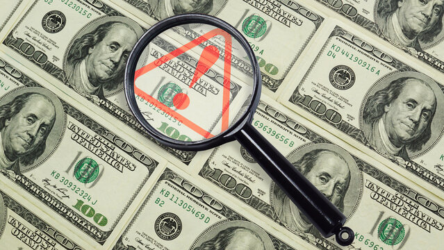 Financial risk warning and Money risk alert - magnifying glass highlighting danger sign on US dollar bills. Economic risk or inflation