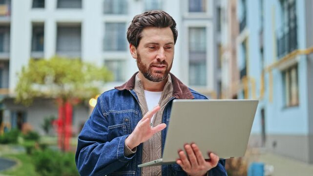 Happy man connects through online video call outdoors, using laptop. Feelings of pleasure and engagement conveyed while talking, highlighting digital communication and modern urban living. - Powered by Adobe