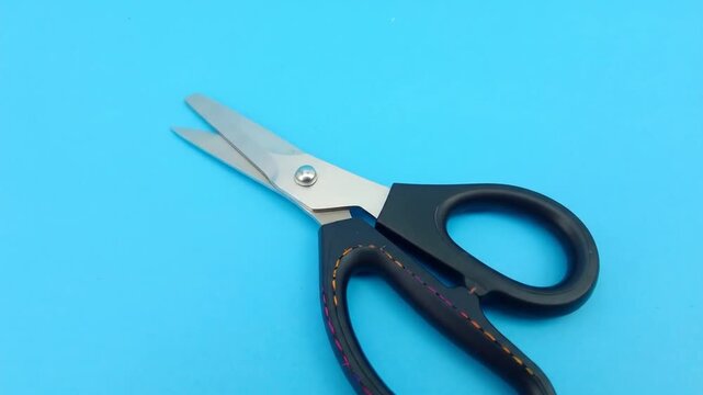 Close-up of open shears with black handles and stainless steel blades set against a blue background