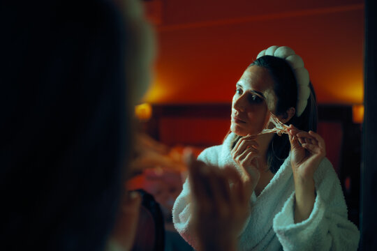  Woman Peeling off a Face Mask Looking in the Mirror. Happy Lady uses rejuvenation products on her skin at home
