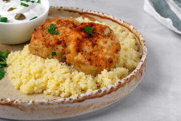 Haddock fish cakes made of mince served with couscous and sour cream sauce on ceramic plate