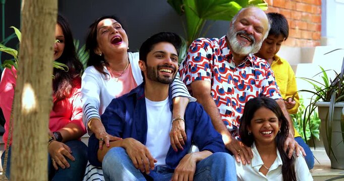Indian family smiling on steps outdoors spending quality time together on green lawn, cheerful multi-generation portrait of grandparents, parents, and kids bonding, relaxing, enjoying leisure weekend