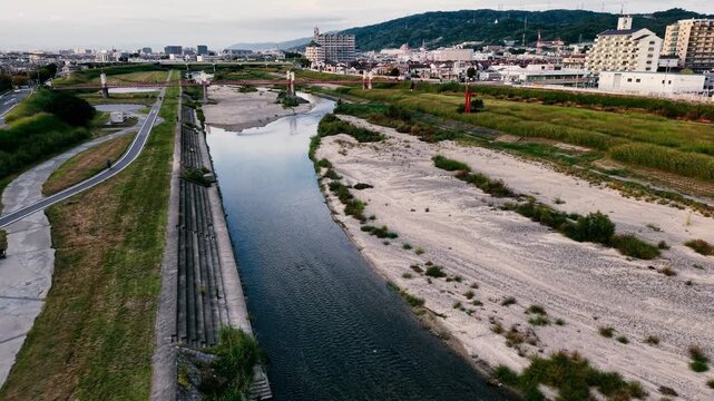 【日本の都市と自然】夕暮れ時の河川敷と街並みを映すドローン空撮（プッシュバック&上昇）
